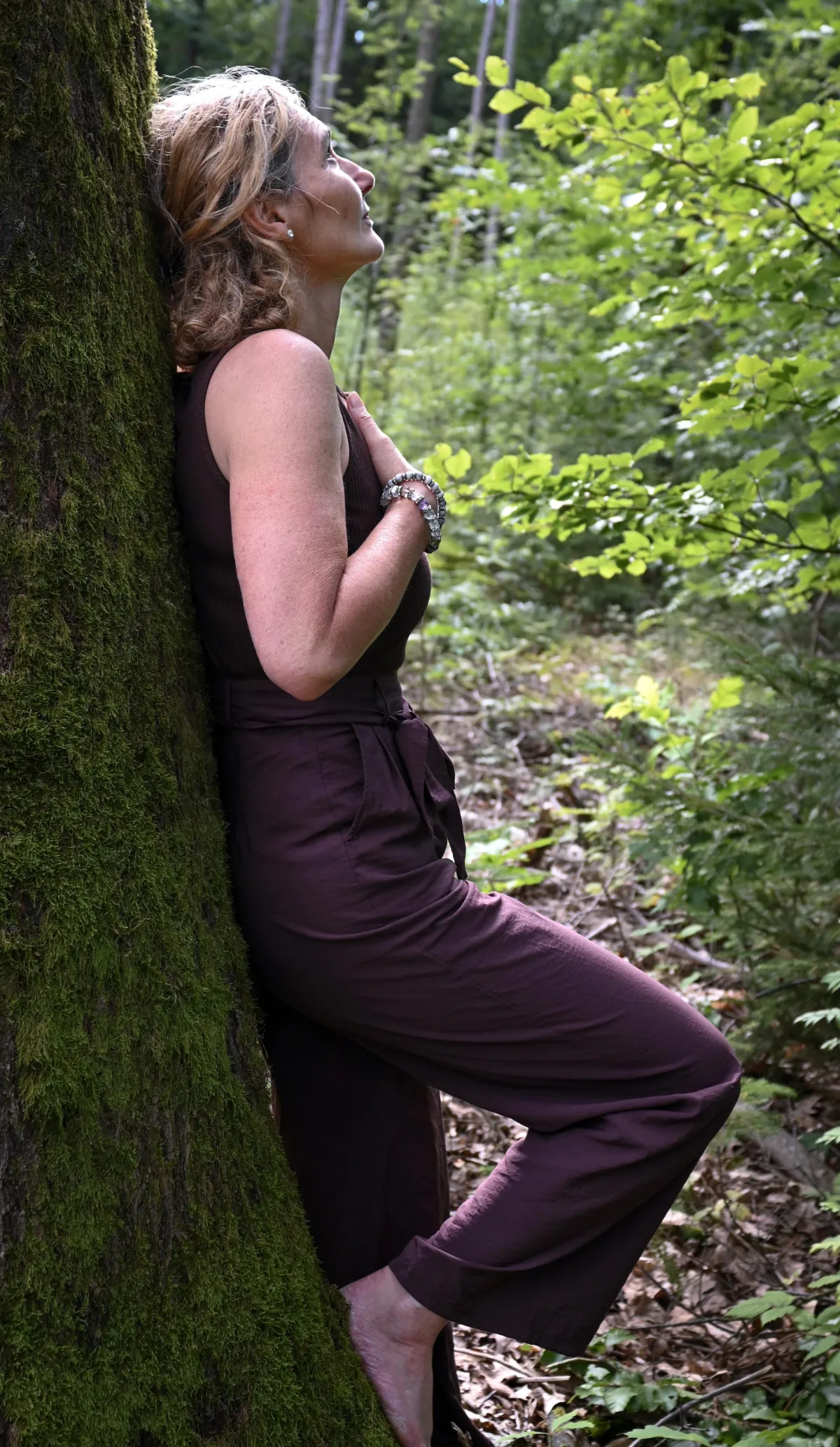 Martina Schneider-Just im Profil, im Wald. Sie lehnt sich mit dem Rücken an einen Baum.