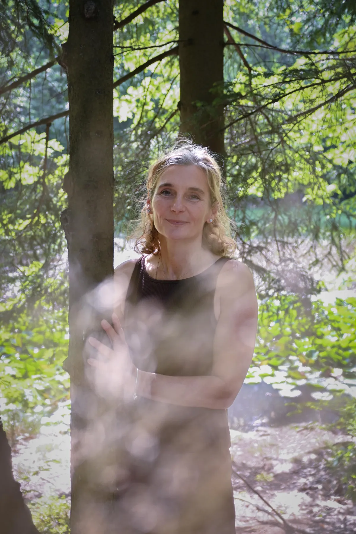 Porträt von Martina Schneider-Just in Dreiviertelansicht. Sie steht in einem Wald neben einem Baum.