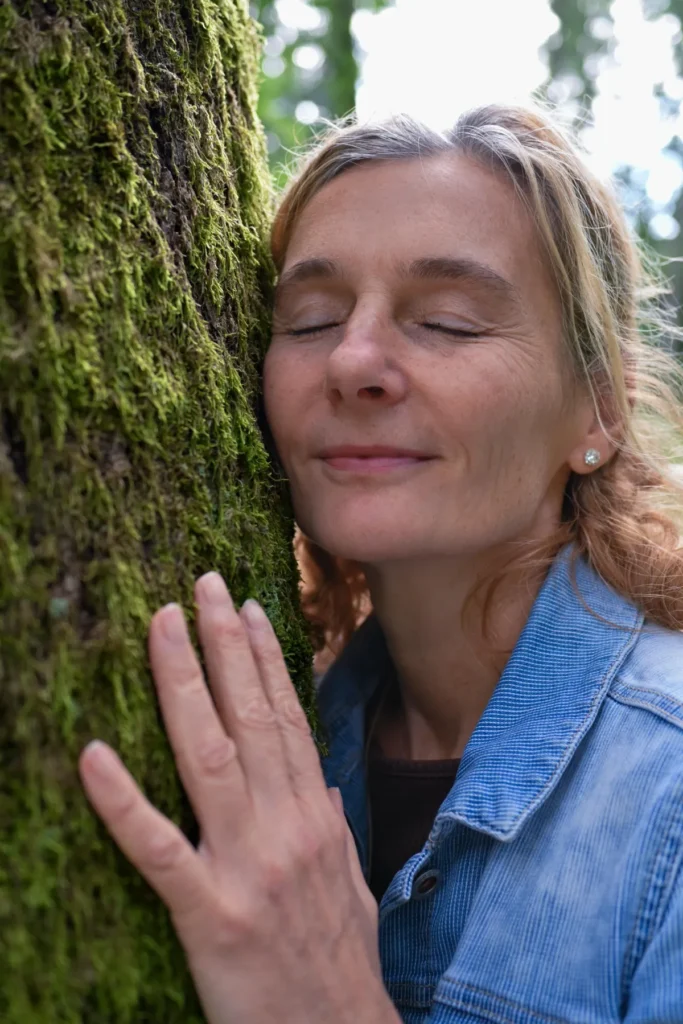 Porträt Martina Schneider-Just. Sie lehnt mit der Wange an einem Baum und hat die Augen geschlossen.
