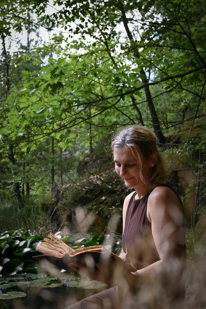 Porträt Martina Schneider-Just. Sie sitzt im Wald und liest in einem Buch.