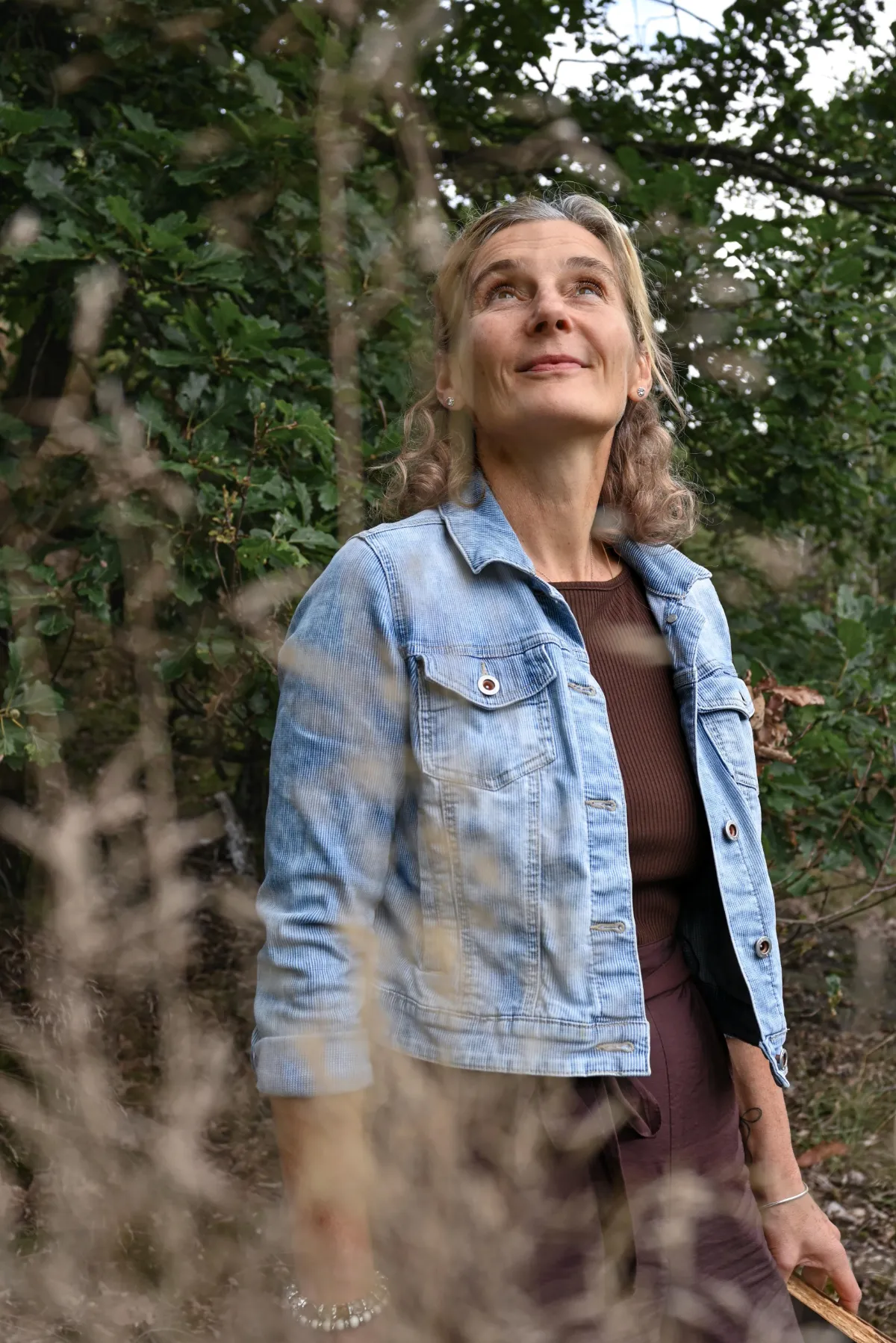 Dreiviertelporträt Martina Schneider-Just. Sie steht im Wald und blickt in den Himmel.